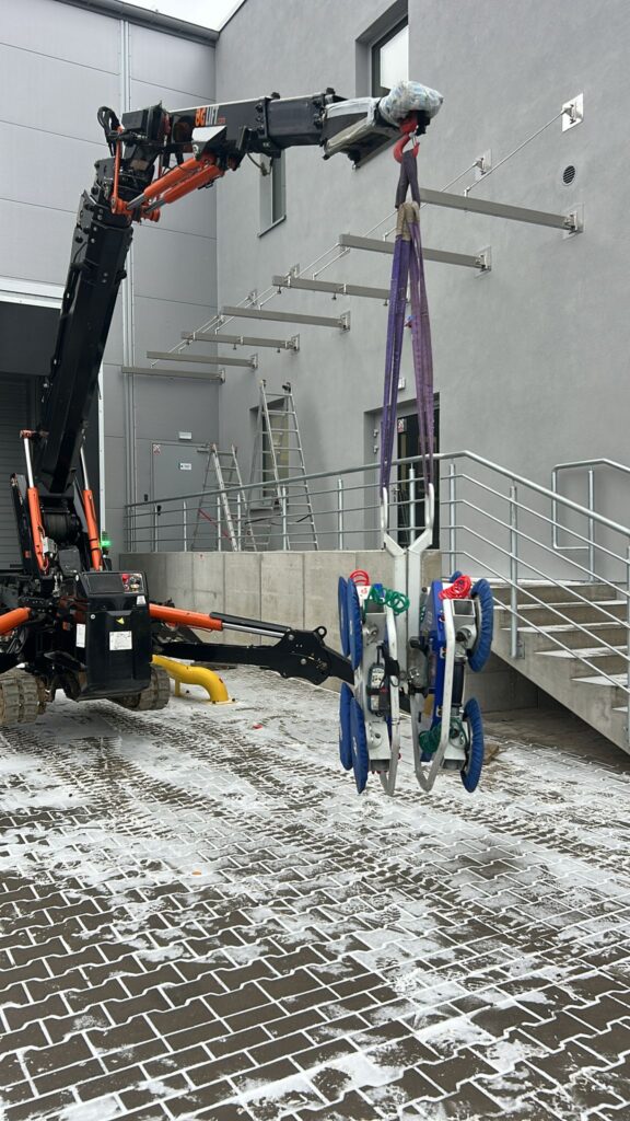 Mini żuraw BGLIFT M250 podczas precyzyjnego montażu dużego przeszklenia z wykorzystaniem profesjonalnych ssawek próżniowych w zimowych warunkach na terenie Wrocławia.