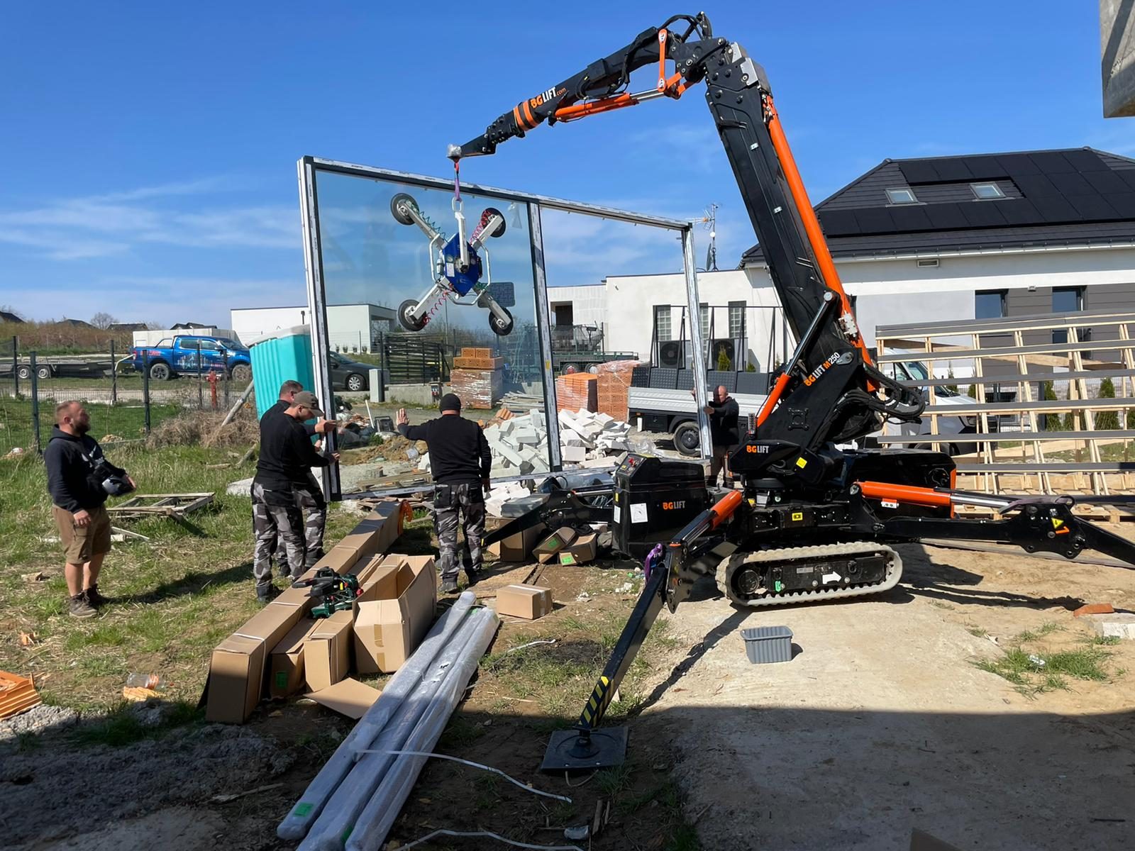 Mini żuraw BG Lift M250 podnosi ssawką próżniową dużą ramę okienną z szybą na budowie domu w Trzebnicy