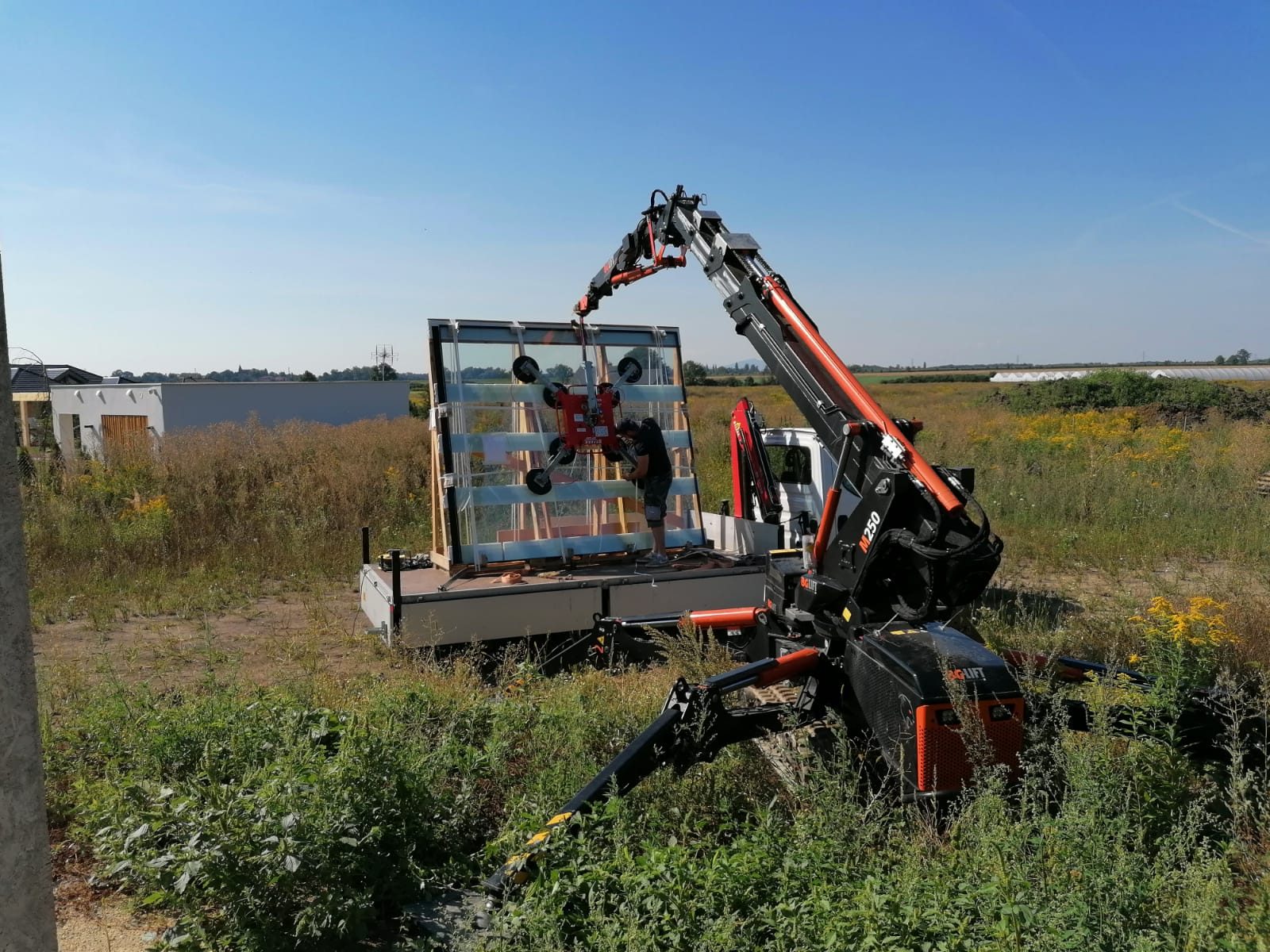 Mini żuraw BG Lift M250 zdejmuje szybę ssawką próżniową z samochodu dostawczego na budowie domu w Mokronosie Górnym